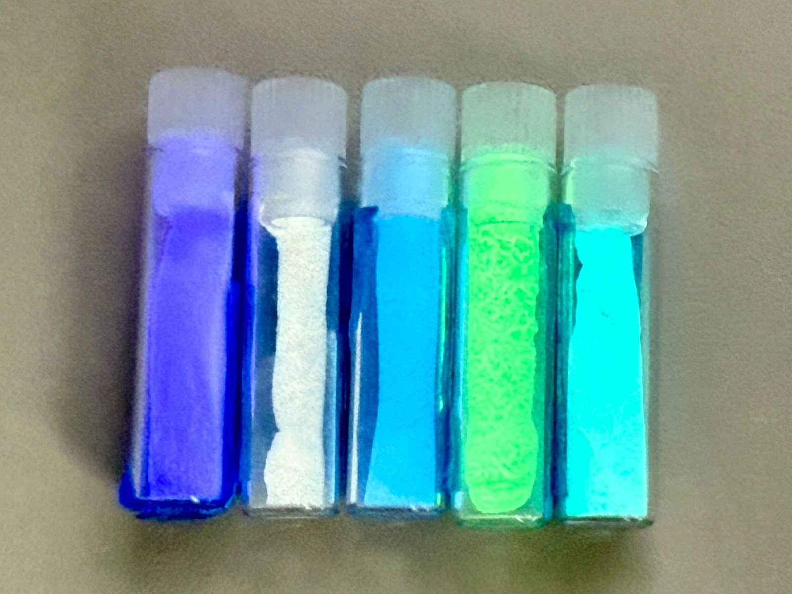 five transparent vials of glowing powder